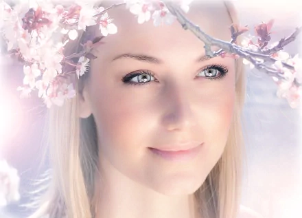 HD desktop wallpaper featuring a close-up of a woman's face, framed by delicate cherry blossom branches with soft, glowing light in the background.