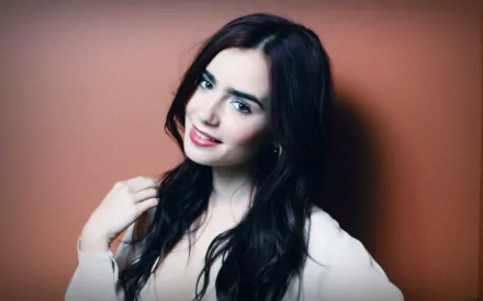 Lily Collins poses confidently against a warm orange backdrop in this HD desktop wallpaper, showcasing her captivating beauty and charm.