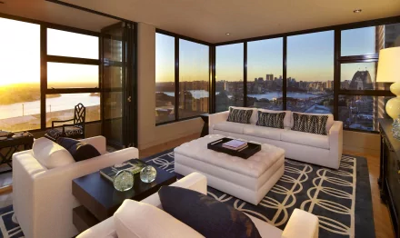 A modern, man-made room with large windows overlooking a city skyline at sunset, featuring white sofas and a patterned rug, captured in 4K Ultra HD for a PC desktop wallpaper.