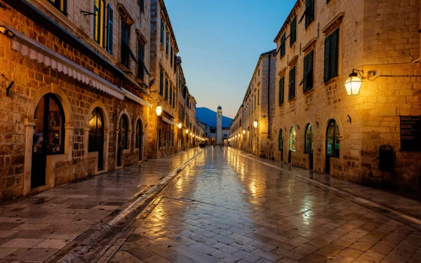 HD desktop wallpaper showcasing a man-made street scene in Dubrovnik with historic stone buildings and warm streetlights reflecting on wet pavement at dusk.