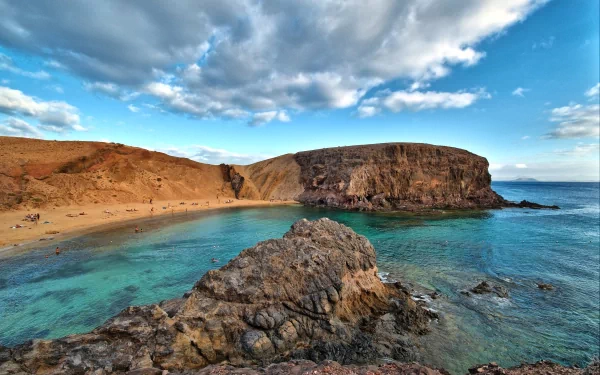 4K Ultra HD desktop wallpaper showcasing a serene coastline with rocky cliffs, clear turquoise water, and a partly cloudy sky under natural light.