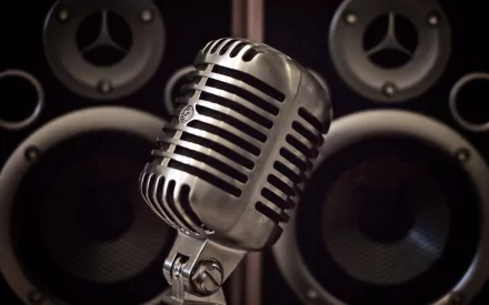 A vintage microphone stands in front of sleek speakers, creating a striking music-themed desktop wallpaper. The image highlights a blend of classic design and modern sound.