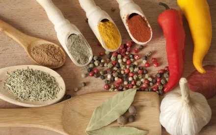 HD desktop wallpaper featuring a vibrant assortment of herbs and spices, including dried seeds, colorful ground powders, whole peppercorns, chili peppers, garlic, and bay leaves.