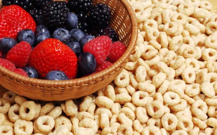 HD PC desktop wallpaper background: woven basket of strawberries and blueberries resting on a bed of round oat cereal — colorful breakfast food.