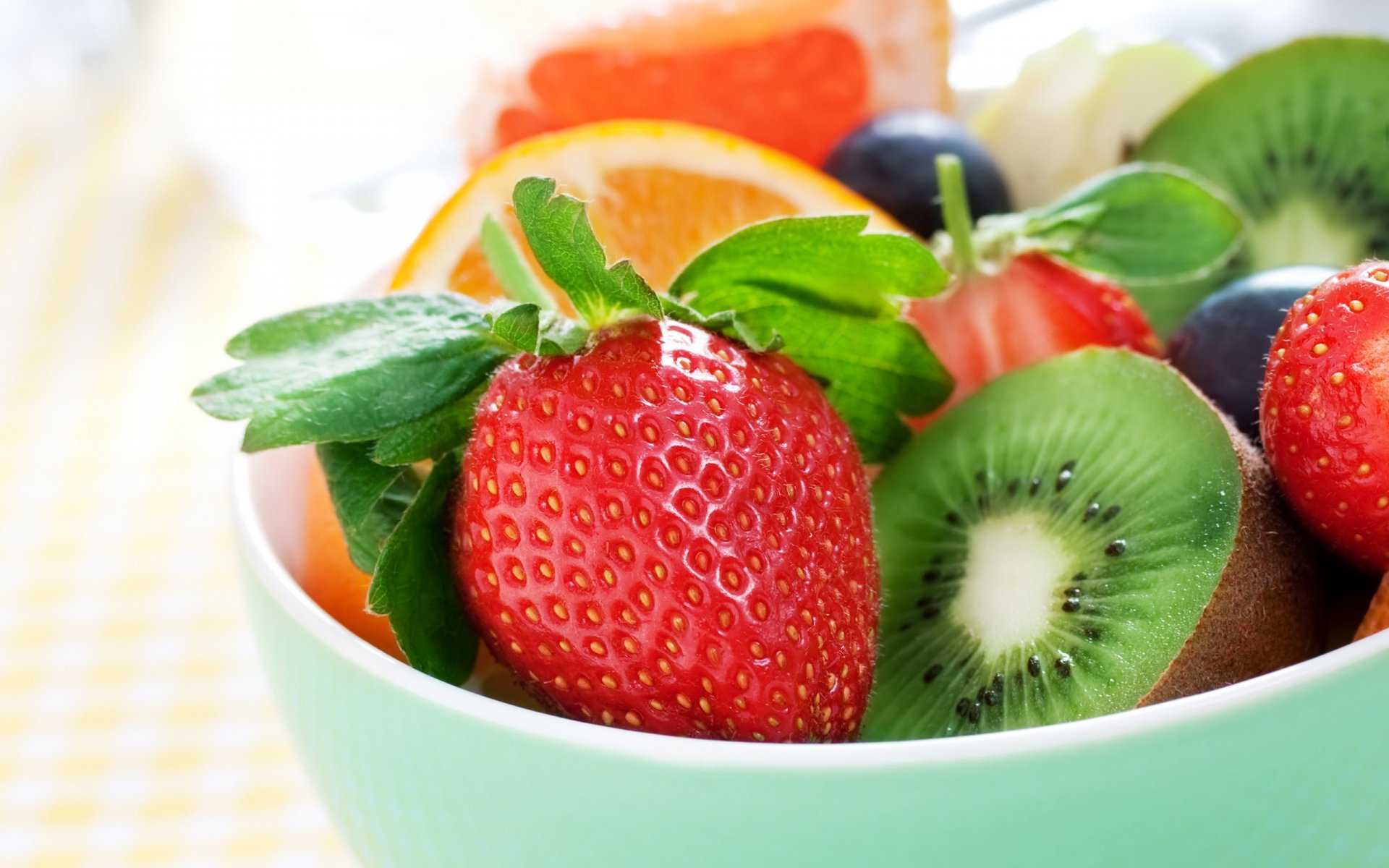 2K Quad HD PC desktop wallpaper background of fresh food/fruit: vibrant strawberries, kiwi, orange slices and blueberries in a mint-green bowl.