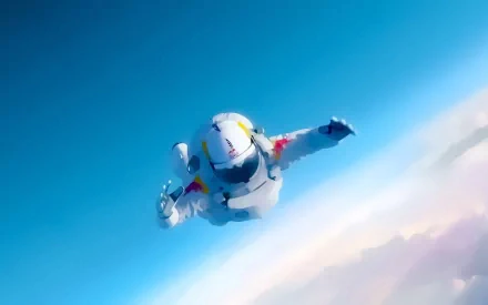 An artistic HD desktop wallpaper showing a skydiving astronaut soaring through a bright blue sky, featuring Red Bull branding and dynamic motion.
