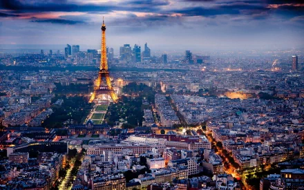 HD desktop wallpaper of Paris, France, showcasing an illuminated Eiffel Tower amidst a sprawling cityscape at twilight, with a dramatic sky in the background.