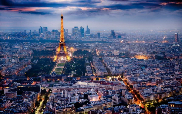 HD desktop wallpaper of Paris, France, showcasing an illuminated Eiffel Tower amidst a sprawling cityscape at twilight, with a dramatic sky in the background.