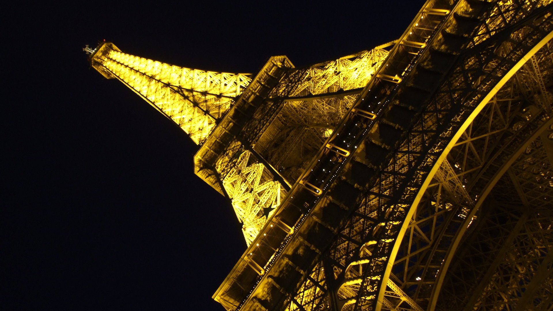 HD desktop wallpaper featuring a close-up, illuminated view of the man-made Eiffel Tower against a dark night sky.