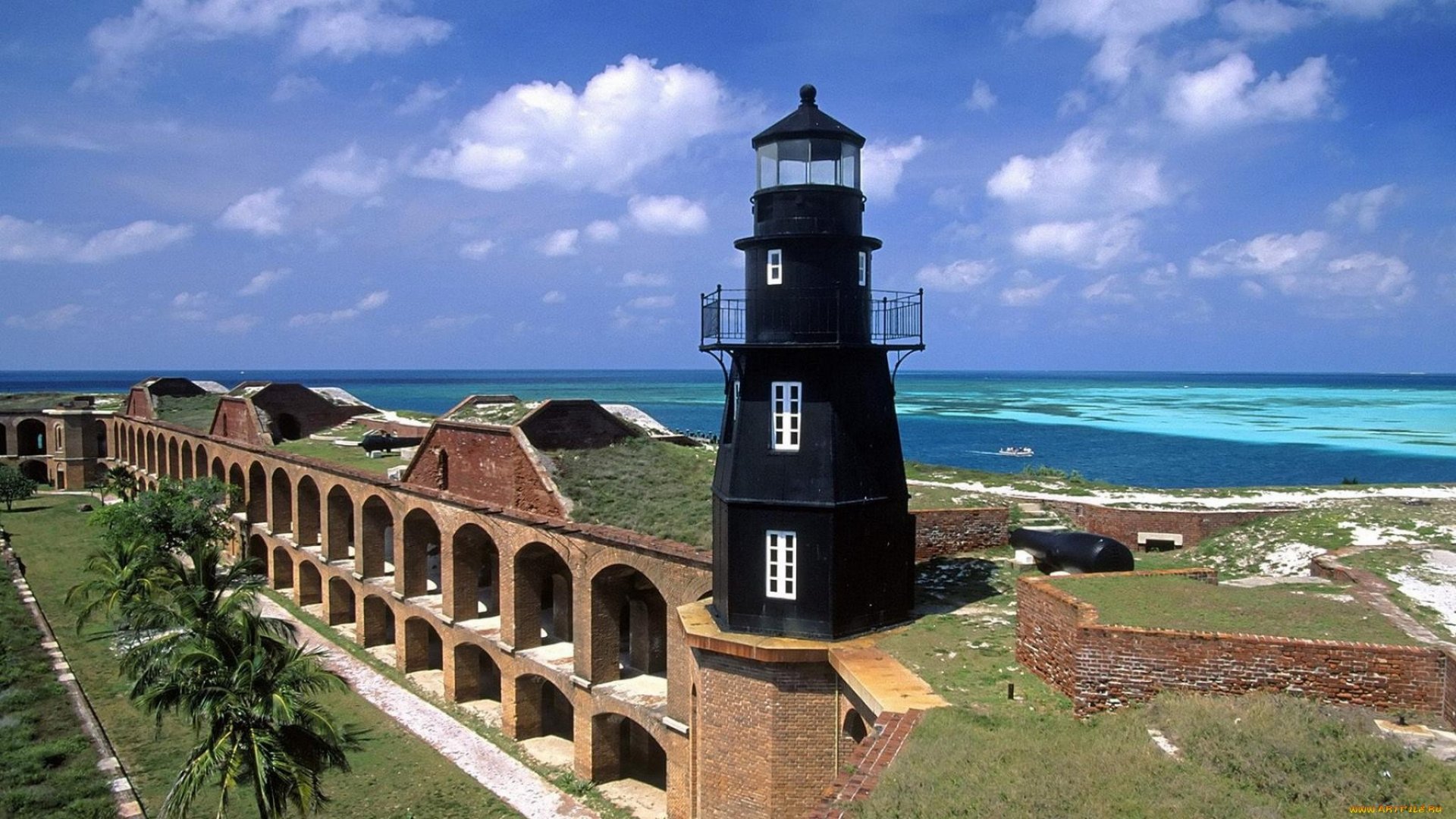 A stunning view of a black lighthouse overlooking turquoise waters in Florida, surrounded by historic man-made structures under a bright blue sky.