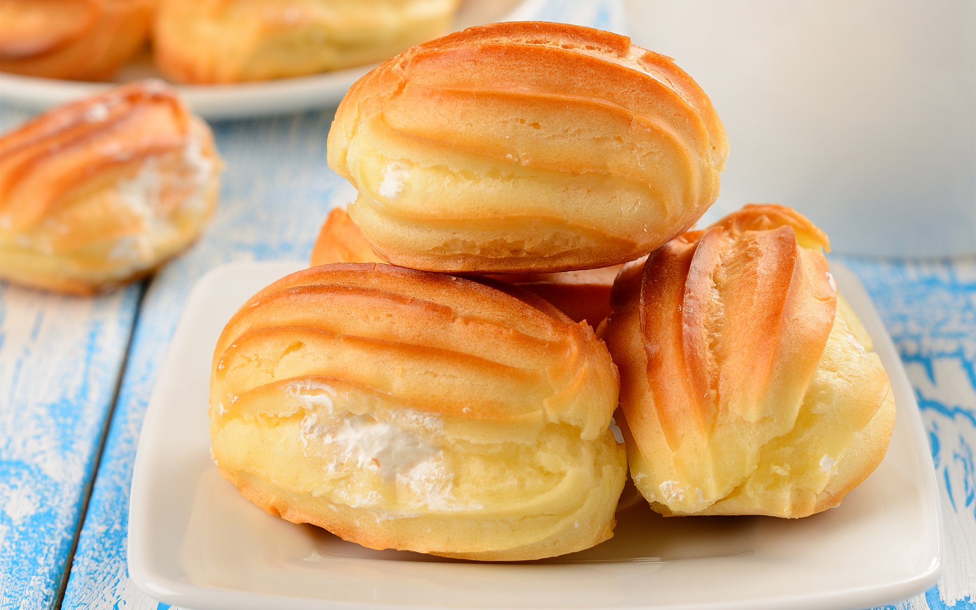 HD desktop wallpaper featuring freshly baked cream-filled pastries stacked on a white plate, showcasing golden, flaky textures against a soft, blurred background.