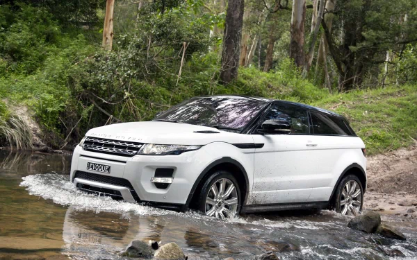 A white Range Rover Evoque navigating through a stream in a lush forest, showcasing its rugged design in this HD PC desktop wallpaper and background.