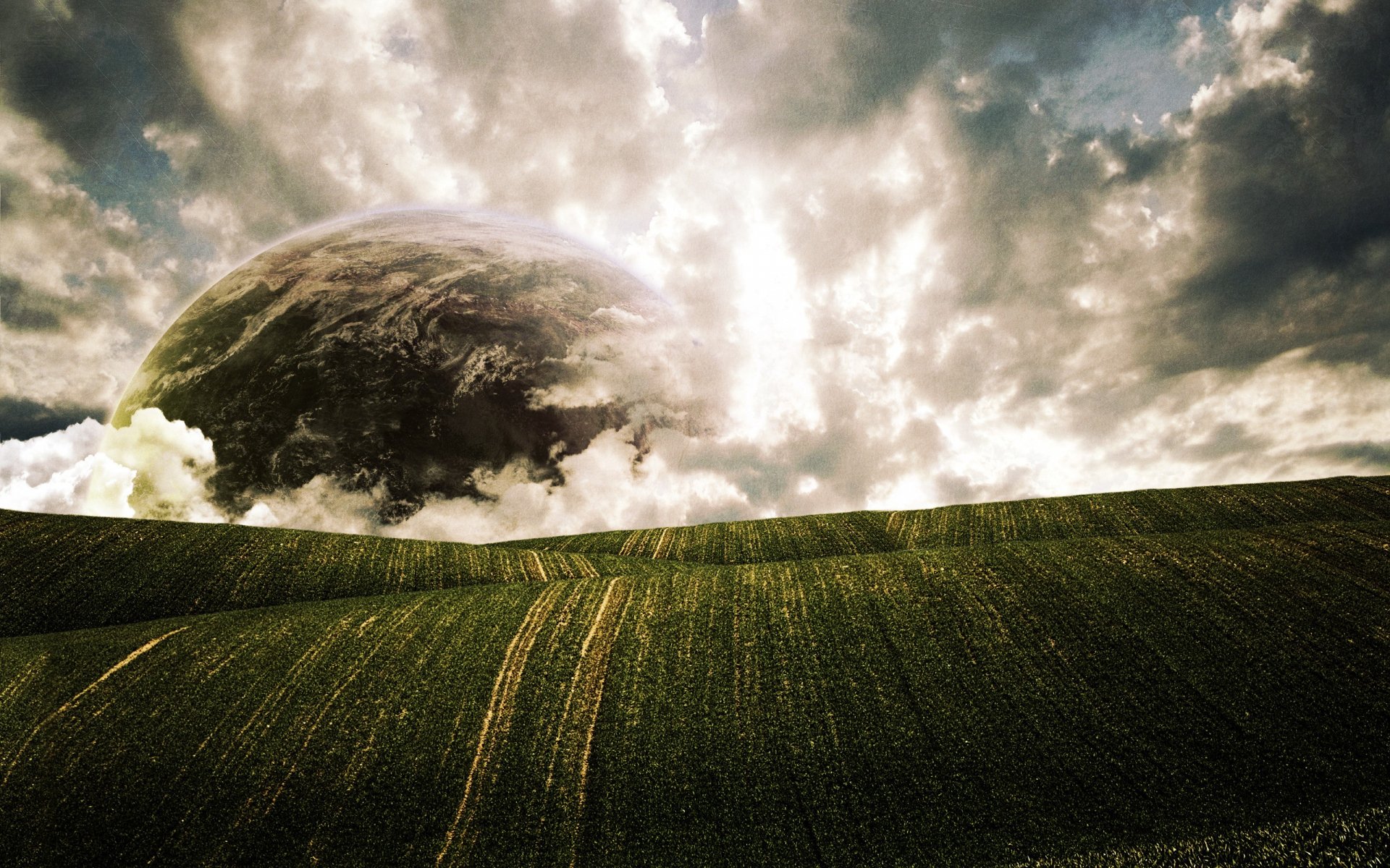 A dramatic nature scene featuring a lush green field under a sky filled with swirling clouds and a distant planet, creating a striking HD desktop wallpaper.