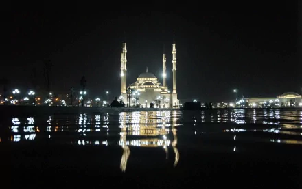 Night view of a beautifully illuminated mosque reflecting on calm water, captured as a high-definition PC desktop wallpaper with a serene religious atmosphere.
