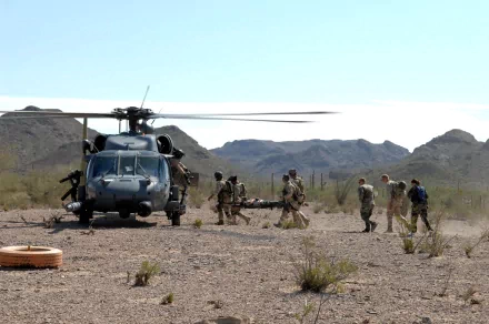 Military personnel carry a stretcher near a Sikorsky HH-60 Pave Hawk helicopter in a desert landscape, captured in this HD PC desktop wallpaper and background.
