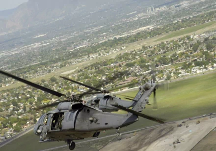 HD desktop wallpaper featuring a Sikorsky HH-60 Pave Hawk military helicopter flying low over a suburban area with a mountain backdrop.