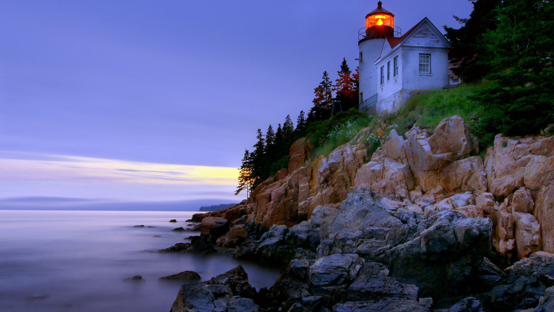 HD desktop wallpaper featuring a man-made lighthouse perched on rocky cliffs at dusk, overlooking a calm sea with a serene sky.