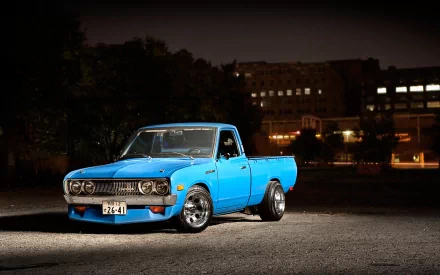 Blue 1974 Datsun 620 pickup parked at night under dramatic lighting against a cityscape — HD PC desktop wallpaper and background.