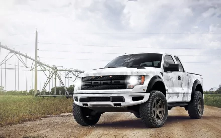 HD desktop wallpaper featuring a white Ford Raptor truck parked on a dirt road with power lines and cloudy sky in the background.