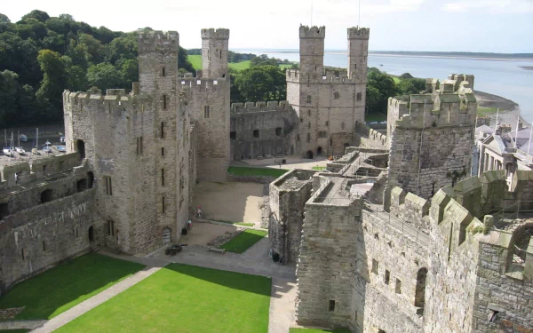 A high-definition desktop wallpaper showcasing the man-made Caernarfon Castle with its stone towers and walls overlooking a scenic waterfront.