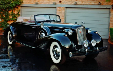 HD PC desktop wallpaper showing a glossy black Cadillac V16 convertible vehicle parked before garage doors, its polished body reflected on wet pavement.