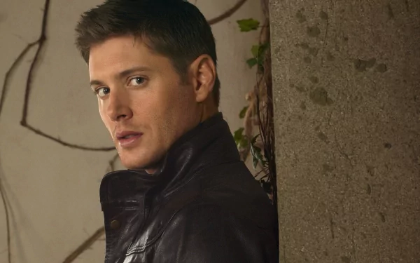 Jensen Ackles poses confidently against a textured wall, showcasing a striking expression. This 4K Ultra HD image serves as an engaging desktop wallpaper and background.