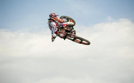 A motocross rider performs an aerial stunt against a blue sky, showcasing the thrill of the sport in this vibrant HD PC desktop wallpaper and background.