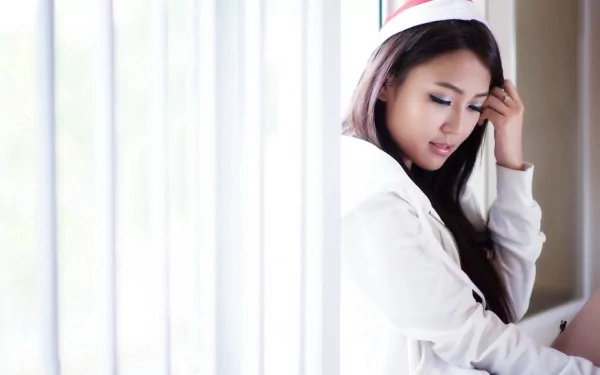 Asian woman in a Santa hat, sitting pensively by a window with white blinds. HD desktop wallpaper and background.