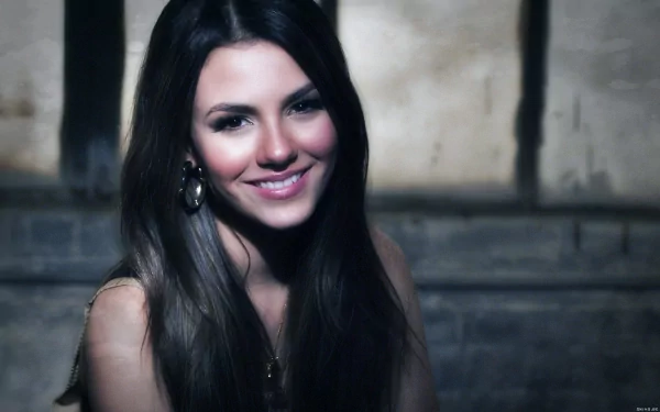 A vibrant HD wallpaper featuring Victoria Justice smiling softly against a textured background, showcasing her charm and warmth.