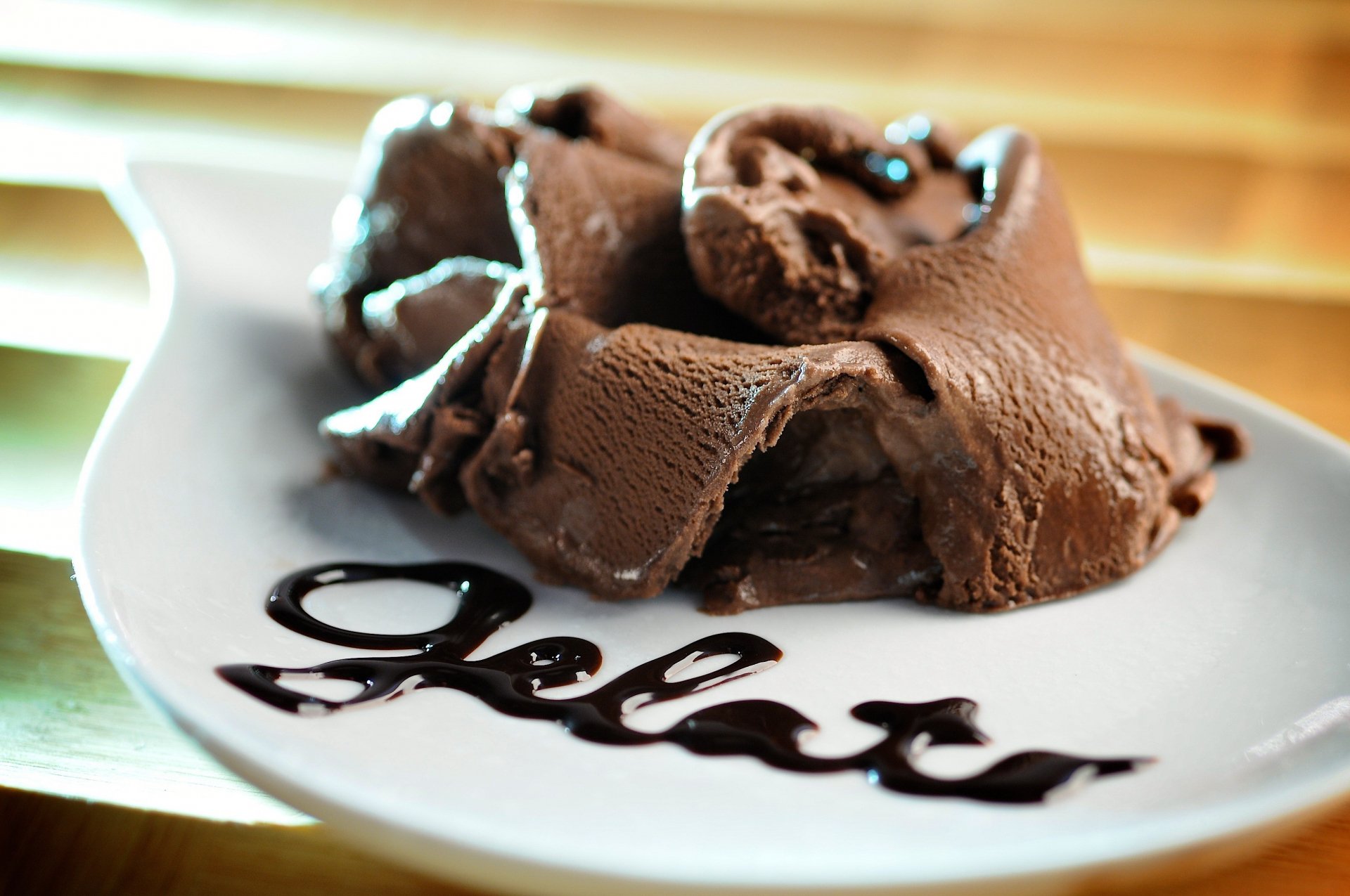 HD PC desktop wallpaper featuring rich, creamy chocolate ice cream artfully served on a white plate with the word gelato written in chocolate syrup.