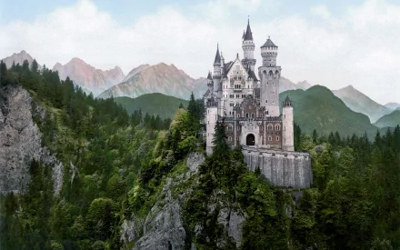 HD wallpaper of Neuschwanstein Castle, featuring a majestic man-made structure perched on a rugged hilltop, surrounded by lush forest with mountain peaks in the background.