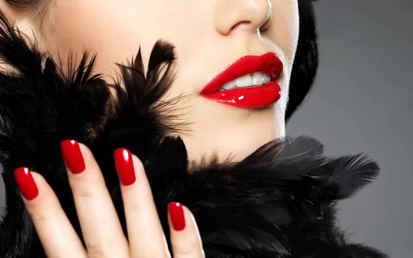 A close-up of a woman's lips adorned with vibrant red lipstick, complemented by striking red nails and a black feather accessory, set against a smooth gray background. 4K Ultra HD wallpaper.