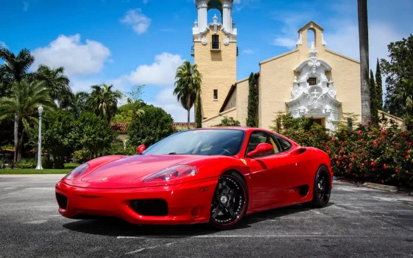 Red Ferrari 360 Modena supercar parked in front of a Mediterranean-style church, vivid HD desktop wallpaper background of a sleek vehicle under a bright blue sky.