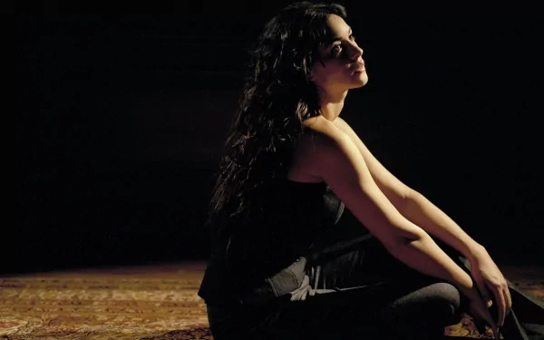 HD desktop wallpaper featuring celebrity Monica Bellucci in a side profile, sitting with arms wrapped around her knees against a dark background.