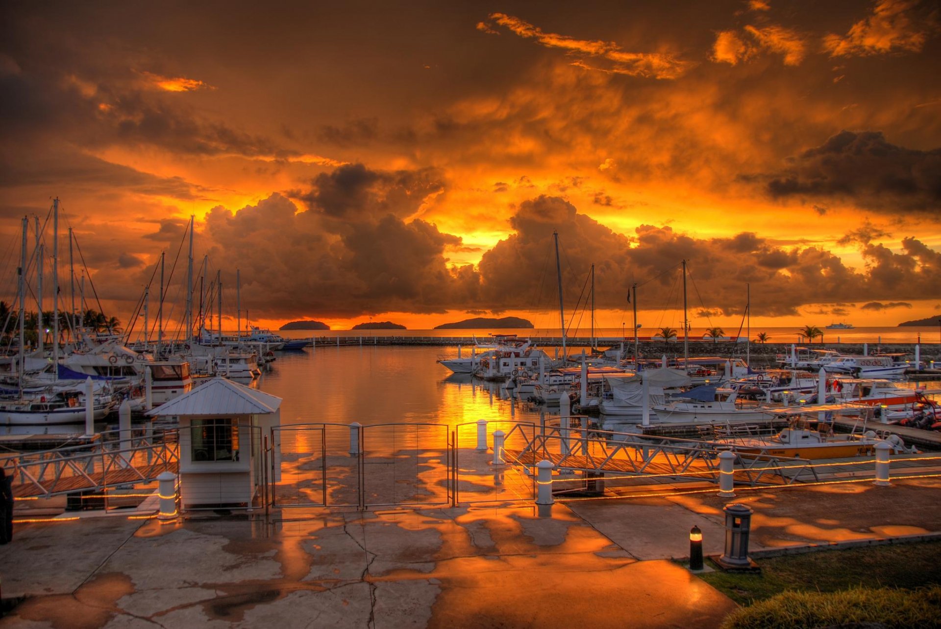 HD desktop wallpaper showcasing a man-made harbor at sunset, with boats docked and dramatic orange clouds reflecting on the water.
