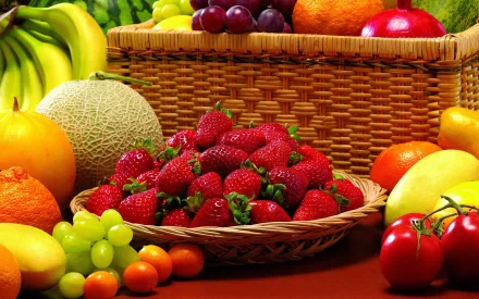 HD desktop wallpaper featuring a vibrant assortment of fresh fruit, including strawberries, bananas, grapes, cantaloupe, oranges, and tomatoes arranged around a wicker basket.