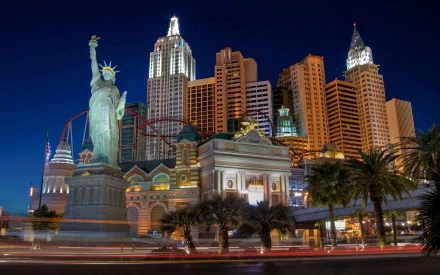 Vibrant nighttime view of Las Vegas, showcasing the iconic skyline with the Statue of Liberty and skyscrapers, set against a rich blue background. A striking casino landscape in HD.