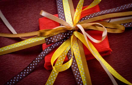A vibrant 4K Ultra HD desktop wallpaper featuring a close-up of a red gift box tied with multiple yellow and brown polka-dot ribbons on a textured surface.