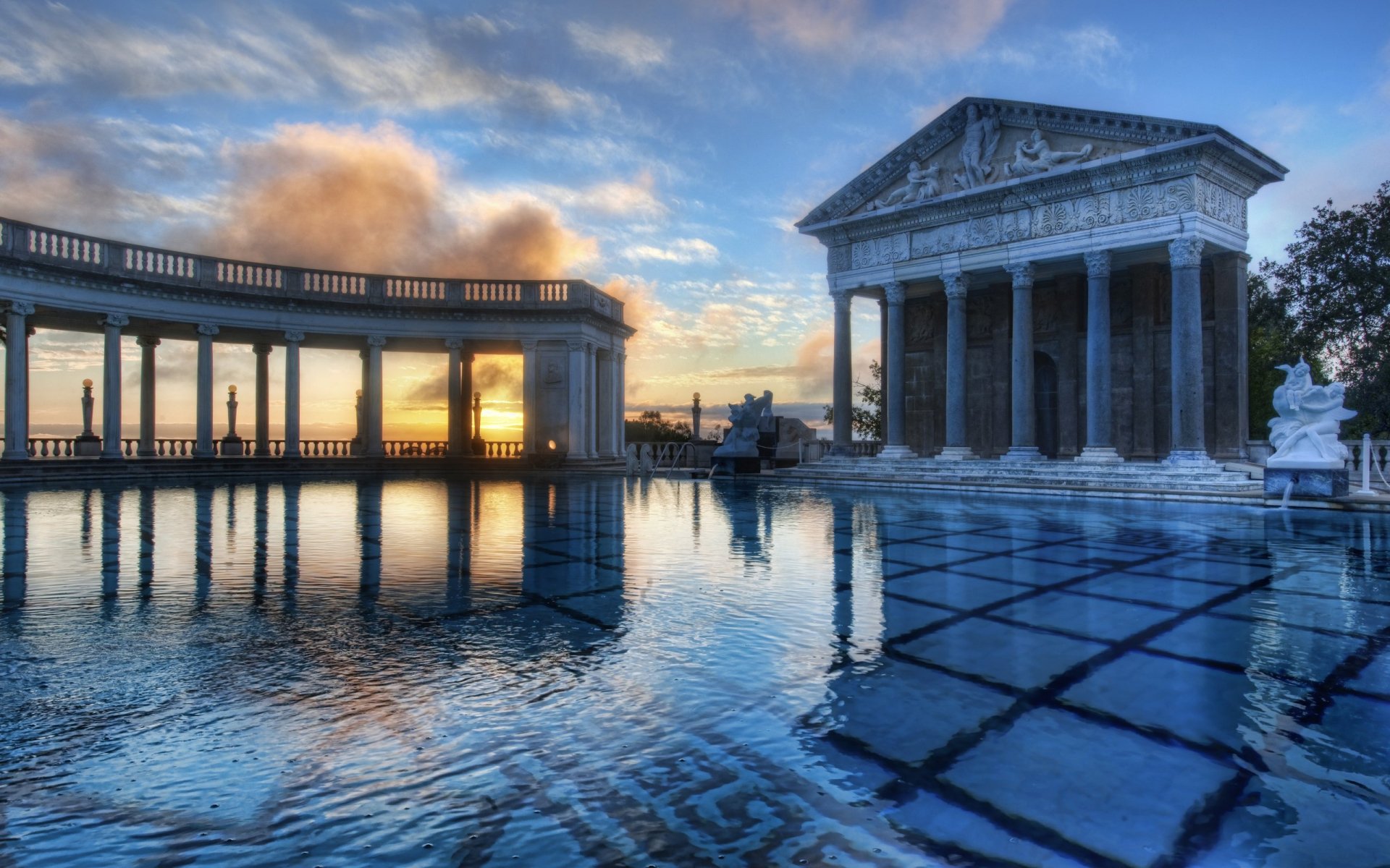 A stunning HD desktop wallpaper featuring the iconic Hearst Castle, showcasing its grand architecture reflected in a tranquil pool at sunset.