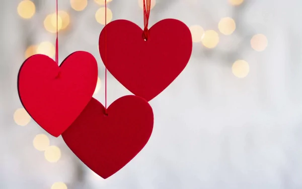 HD PC desktop wallpaper featuring three red hanging hearts against a soft bokeh background, celebrating the Valentine's Day holiday.