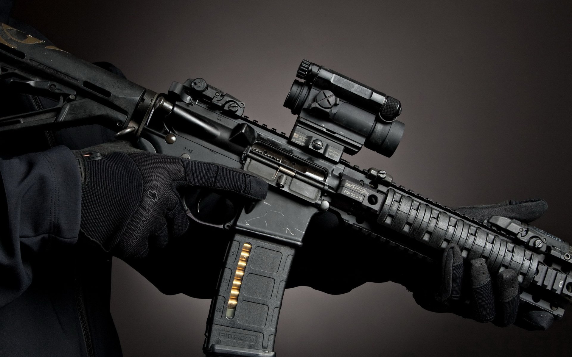 A close-up of a man holding an assault rifle, showcasing its detailed features against a dark background. This high-definition image serves as a striking desktop wallpaper.