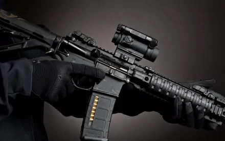 A close-up of a man holding an assault rifle, showcasing its detailed features against a dark background. This high-definition image serves as a striking desktop wallpaper.