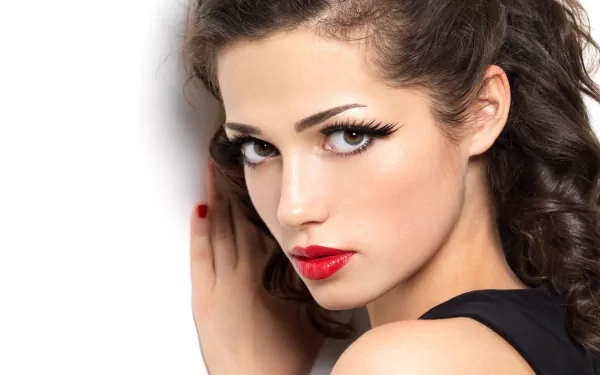 Close-up of a woman’s face with bold makeup, featuring dramatic eyelashes and red lips, set against a clean background; an eye-catching HD desktop wallpaper.