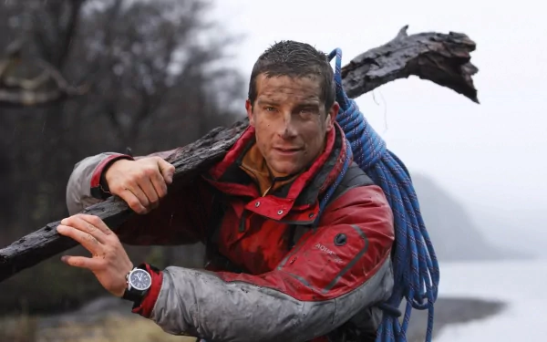 HD desktop wallpaper featuring Bear Grylls, dressed in outdoor gear, carrying a large stick with a coiled rope over his shoulder in a rugged, misty environment.