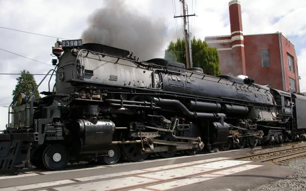 HD desktop wallpaper featuring a detailed black steam locomotive emitting smoke as it rests near industrial buildings and railroad tracks under a cloudy sky.