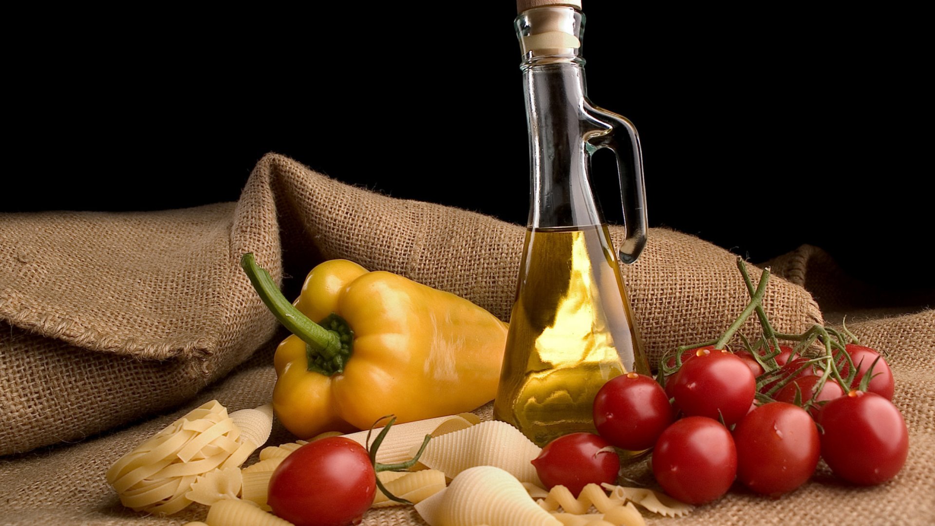 Food still life 2K Quad HD PC desktop wallpaper/background: bottle of olive oil, yellow bell pepper, cherry tomatoes on the vine and conchiglie pasta on burlap with a dark backdrop.