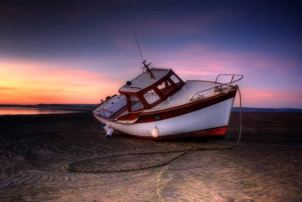 HD PC desktop wallpaper and background of a small beached boat vehicle on wet sand at sunset, purple-orange sky reflecting on its hull.