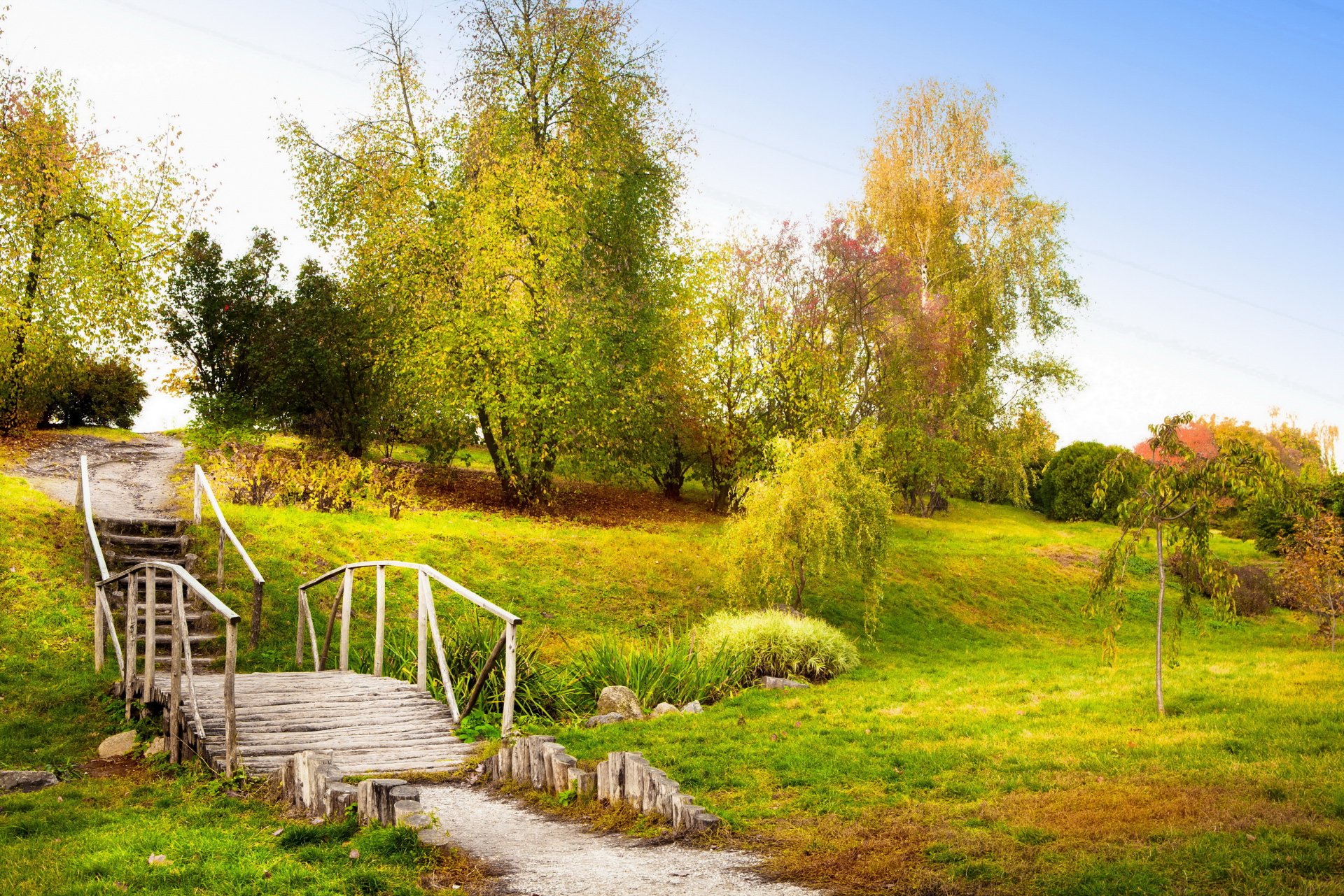 Man-made wooden bridge crossing grassy parkland with trees and bright sky — 2K Quad HD PC desktop wallpaper background.