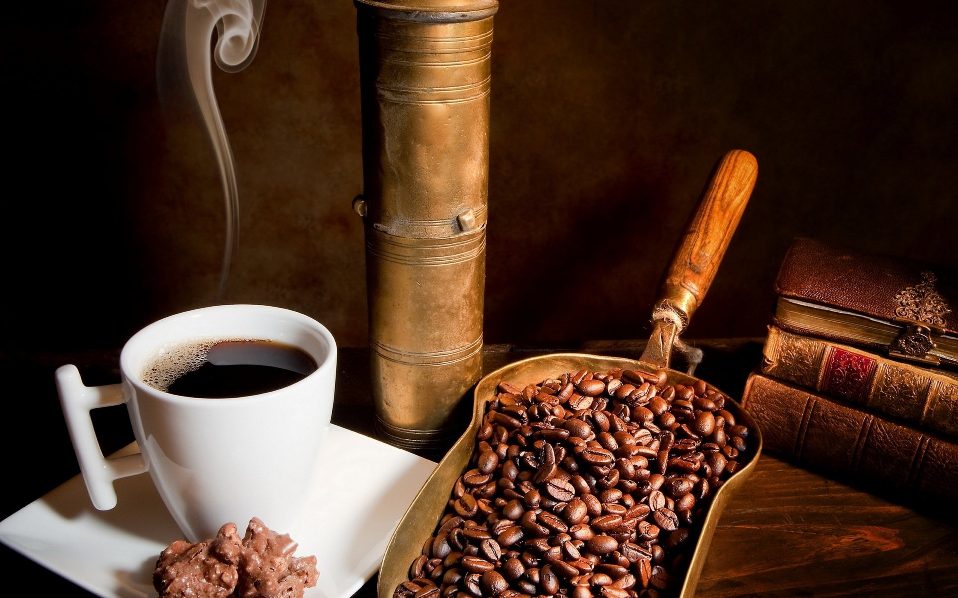 HD PC desktop wallpaper featuring a steaming cup of coffee, roasted coffee beans in a wooden scoop, a vintage coffee grinder, and stacked books on a warm-toned surface.