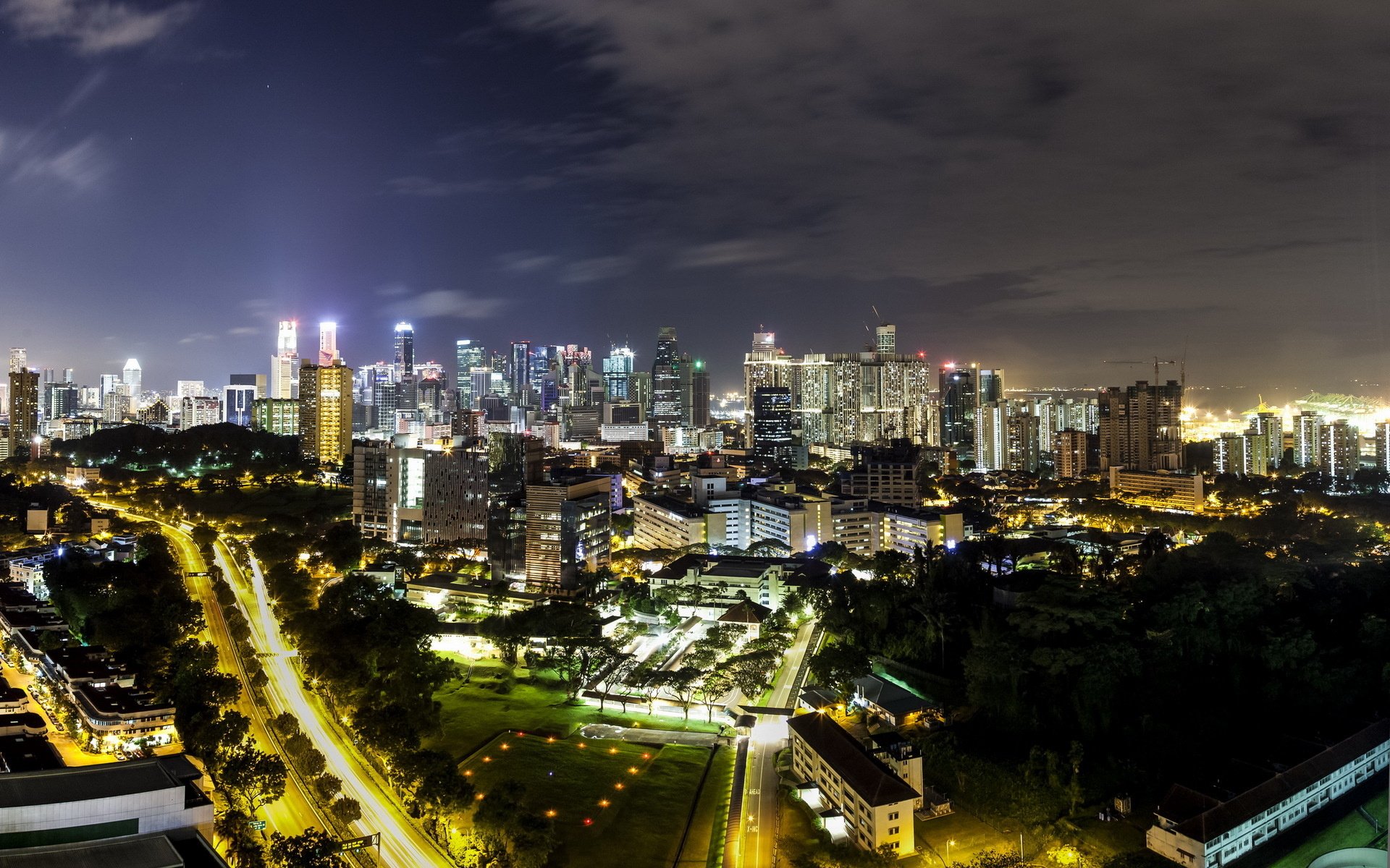 HD PC desktop wallpaper of Singapore man-made night skyline with illuminated skyscrapers, winding roads, and a lit urban park.